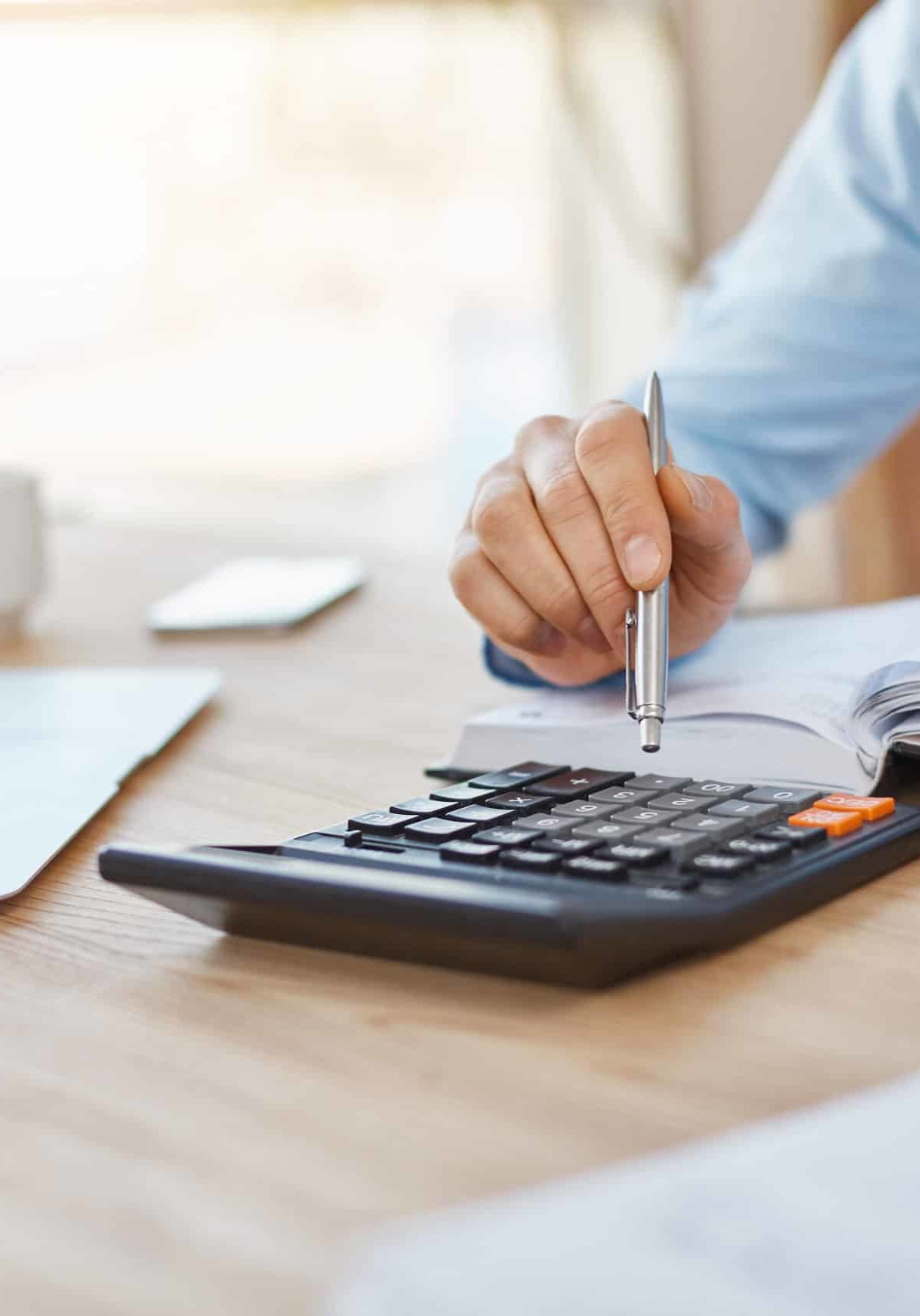 Close up detail of professional serious accountant sitting in light office, checking company finance profits on calculator, writing down results in notebook. Business concept.